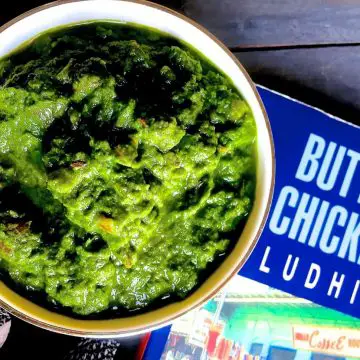 Sarson ka saag, the classic winter curry from the punjab. Shown in a white bowl with a book on Butter Chicken in Ludhiana, alongside