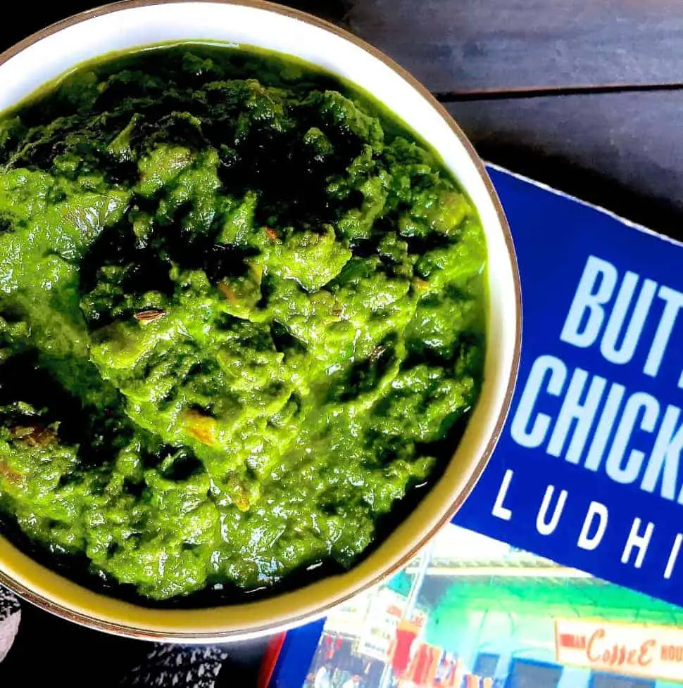 Sarson ka saag, the classic winter curry from the punjab. Shown in a white bowl with a book on Butter Chicken in Ludhiana, alongside