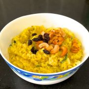 Ven Pongal the delicious tamil version of khichdi. Garnished with fried cashew nuts and raisins, rice and moong dal lentils cooked together with turmeric, served in a white bowl patterned with blue and yellow