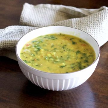 Yellow split Lentils and green spinach stew with red tomatoes, Arhar Dal Palak in a white bowl with a grey green napkin at the back, on a dark wooden surface