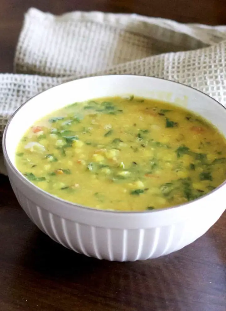 Yellow split Lentils and green spinach stew with red tomatoes, Arhar Dal Palak in a white bowl with a grey green napkin at the back, on a dark wooden surface