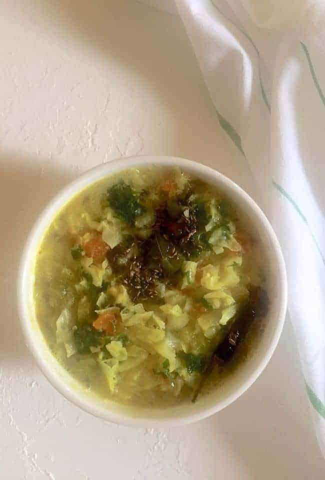 Greenish yellow cabbage stew with a tempering of mustard, chili and cumin and garnish of coriander leaves. On a white background with a green striped white napkin on the side