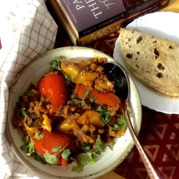 A round plate of stuffed Shimla mirch or coloured bell peppers stuffed with potato mash with a plate of chapatis, books and a checked napkin on the side