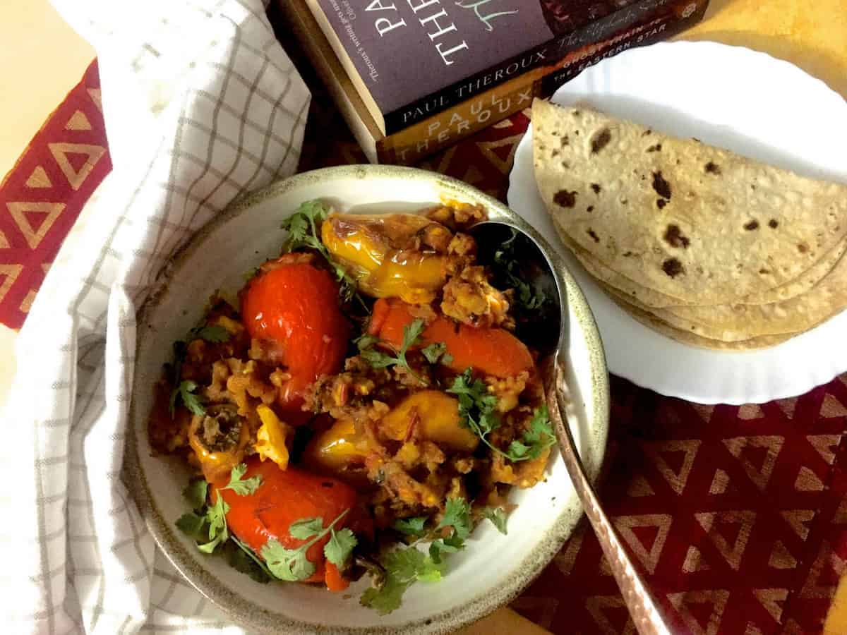 A round plate of stuffed Shimla mirch or coloured bell peppers stuffed with potato mash with a plate of chapatis, books and a checked napkin on the side