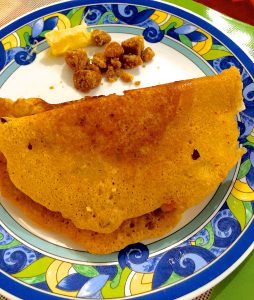 Multigrain adai thick crepes served on a white plate edged in a blue and yellow pattern, with jaggery and butter