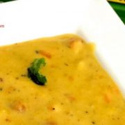 Thick yellow corn chowder with bits of corn seen on the surface, on a white plate. Garnished with mint leaves