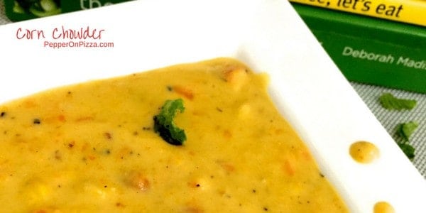 Thick yellow corn chowder with bits of corn seen on the surface, on a white plate. Garnished with mint leaves