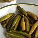 Pointed gourd stuffed with spices and sauteed. On a white plate with a green and yellow rim. Bharwan Parwal