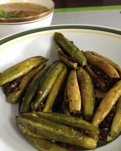 Pointed gourd stuffed with spices and sauteed. On a white plate with a green and yellow rim. Bharwan Parwal