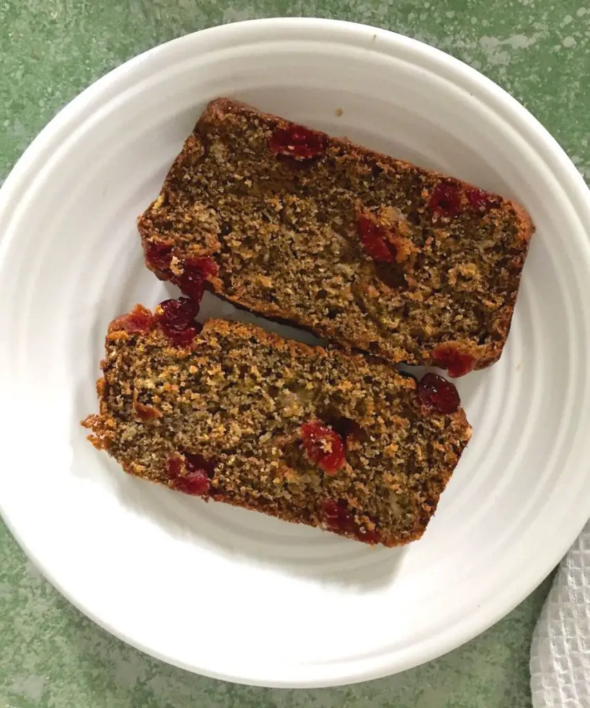 Two slices of banana cranberry bread on white plate, on a green background