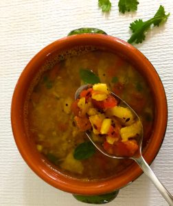 An orange bowl of pineapple rasam with a spoonful of pineapple and tomato pieces
