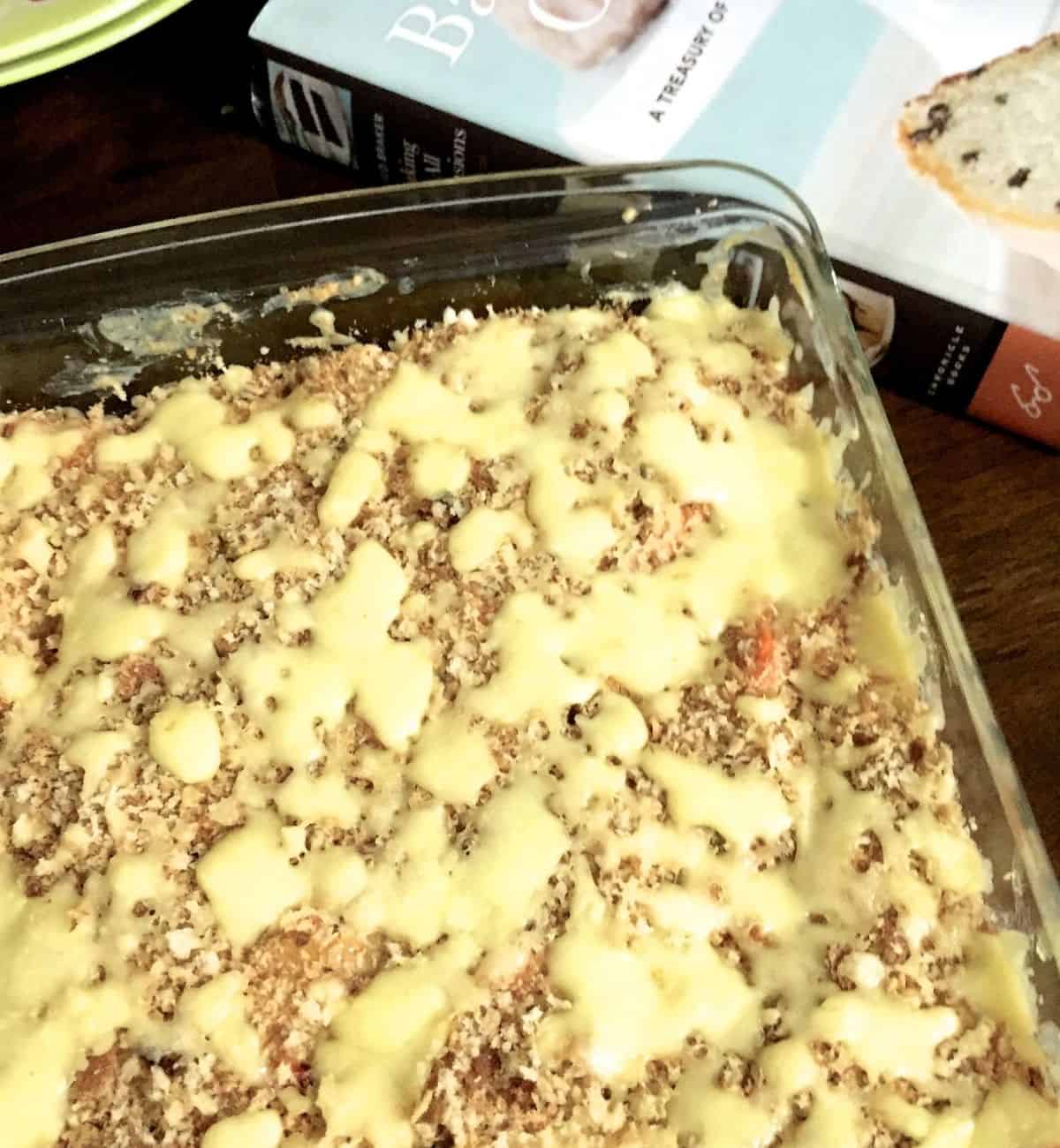 Vegetables baked with cheese in a creamy sauce, vegetable au gratin in a glass baking tray with a blue and brown Baking book to the right