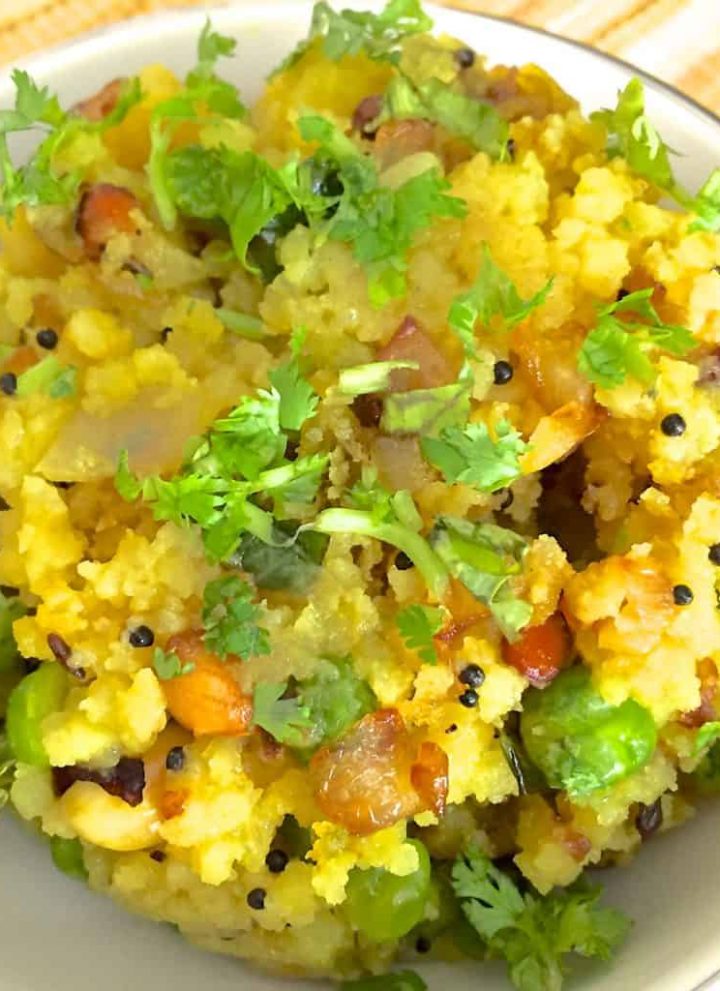 A bowl of bright yellow poha with peas and peanuts garnished with cilantro and tempered with mustard