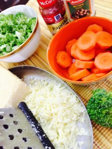 Sliced carrots in an orange bowl, broccoli flowerets and a plate with a block of cheese, a grater and grated cheese_ingredients for Broccoli cheddar soup