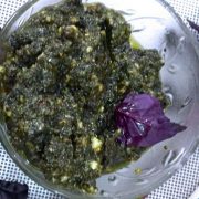 A glass bowl with a greenish Purple Basil Pesto with some Purple basil leaves alongside