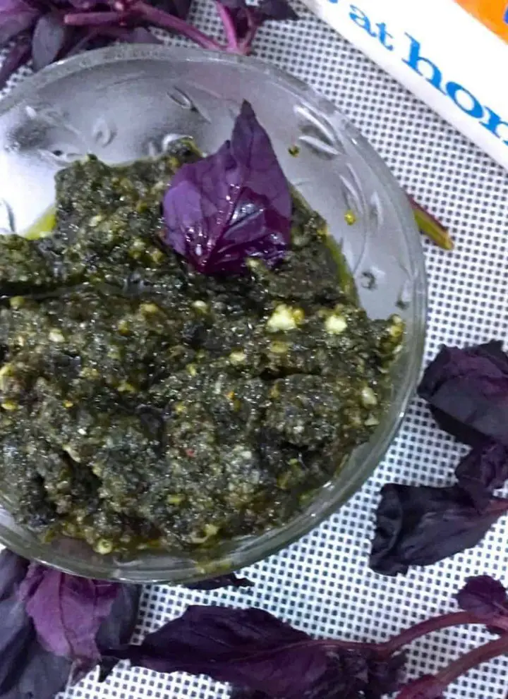 A glass bowl with a greenish Purple Basil Pesto with some Purple basil leaves alongside
