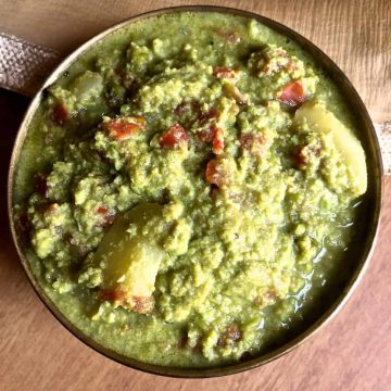 Matar ka Nimona, a fresh green pea and potato curry in a tomato onion spices gravy, in a round brass bowl on a light brown background.