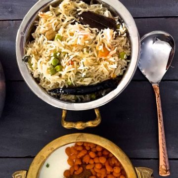 Matar ki Tehri - view from the top of a bowl of Green peas cooked with fragrant Basmati rice and spices, with another bowl with boondi raita and a long bass spoon alongside