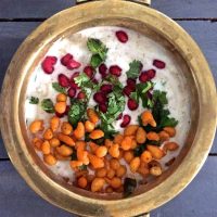 White Boondi Raita in a brass bowl, garnished with chickpea droplets, pomegranate arils and mint leaves