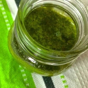 A glass bottle with green homemade basil oil. A green and white napkin in the background