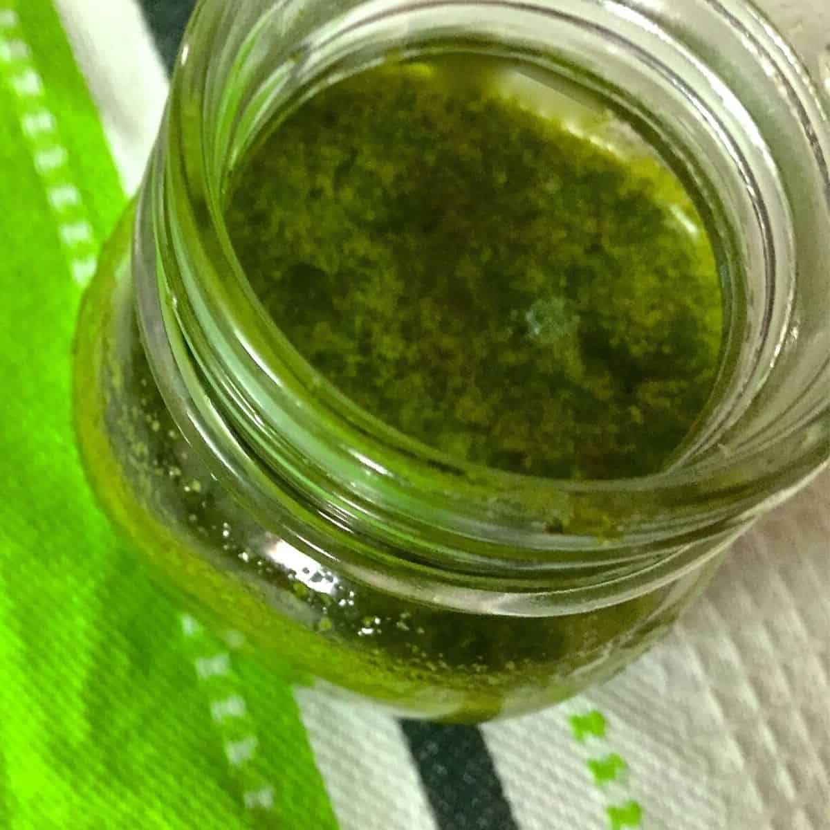 A glass bottle with green homemade basil oil. A green and white napkin in the background