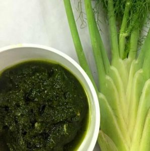 Dark green fennel frond pesto in a white bowl, with fennel showing its fronds, in the background