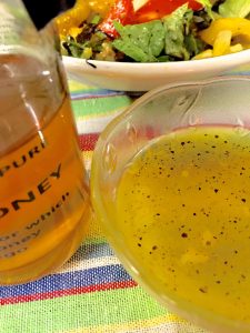 Bottle of honey next to a bowl of honey lemon garlickly salad dressing