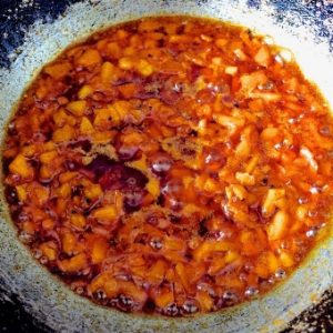 Making Raw Mango relish: a pan with mango slices coloured by the red chili powder, being cooked in oil, turmeric, mustard seeds