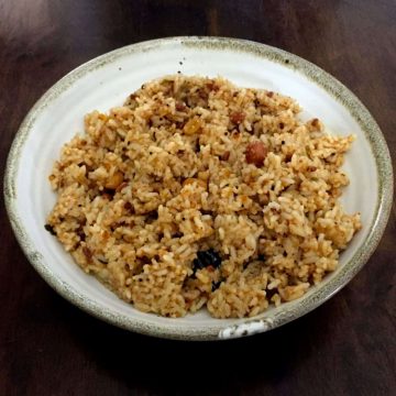Brown hued Puliyodharai Tamarind Rice with peanuts on a white bowl with a thin beige edge, on a dark wooden background
