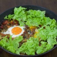 Shakshuka with sauteed red peppers and tomato and egg, surrounded by a bed of green lettuce