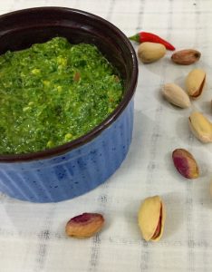 Parsely cilantro pesto in a blue bowl with pista nuts scattered nearby