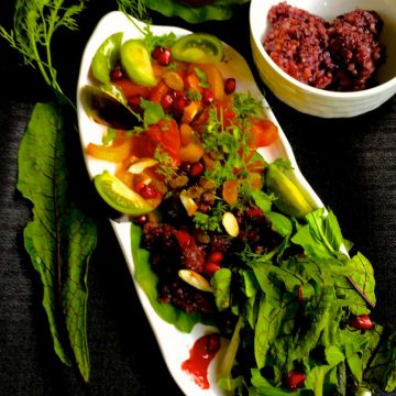 Black Rice Salad with fresh greens and herbs and a cranberry orange dressing on a boat shaped white plate with a white bowl for the dressing