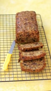 Christmas fruit cake on a cooling rack on a yellow background board with slices of the cake and yellow handled knife alongside