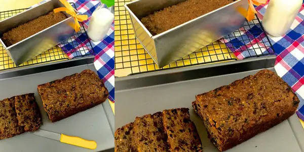 Dark brown Christmas fruit cake partly sliced, with a baking tin with another fruit cake in the background. A red blue and white checked napkin on the right