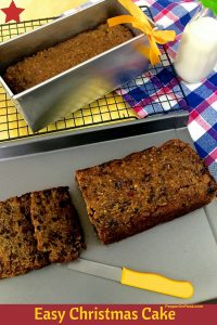 Christmas Fruit cake sliced with a yellow knife and one cake in a pan showing just behind the sliced one