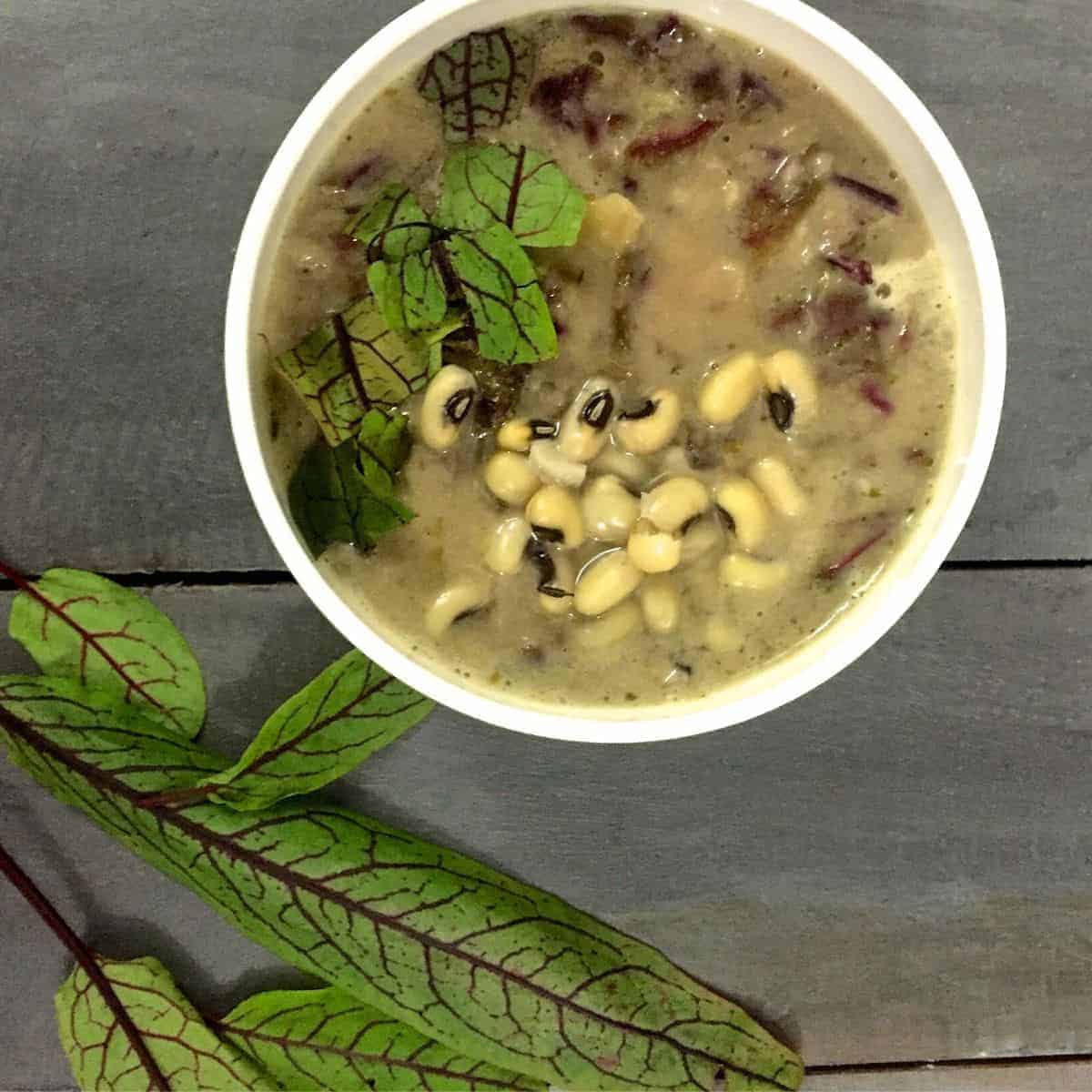 Thick french style 2 bean sorrel soup granished with red sorrel leaves and black eyed peas seen on the surface. Red sorrel leaves in the foreground, all on a wooden background