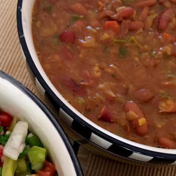 Flavourful Nutritious Rajma Masala Curry of red kidney beans in a thick tomato onion gravy in checkered black and white bowl with salad by the side