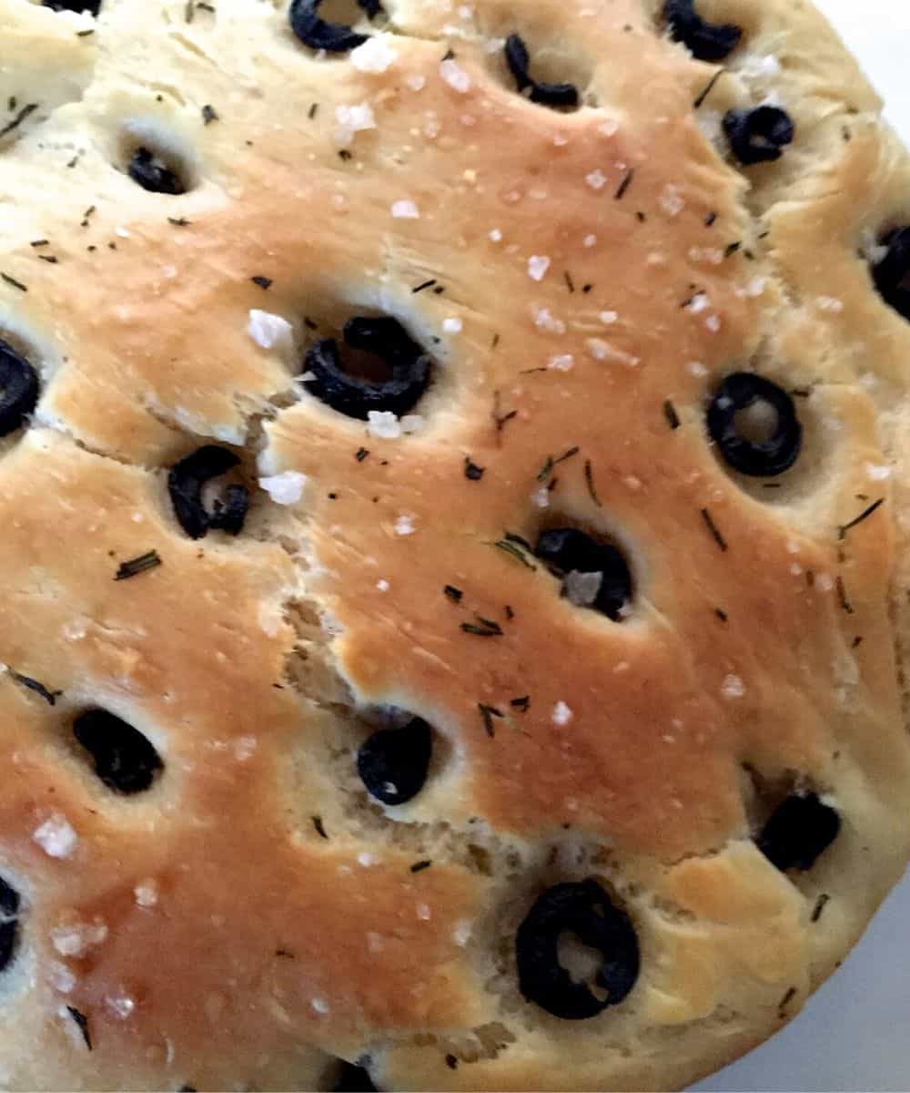 Well baked crusty olive rosemary focaccia with specks of salt seen among the olives and bits of rosemary