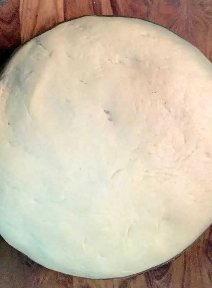 A round sphere of basic Dough for pizza, rising in a glass bowl on a brown wooden background