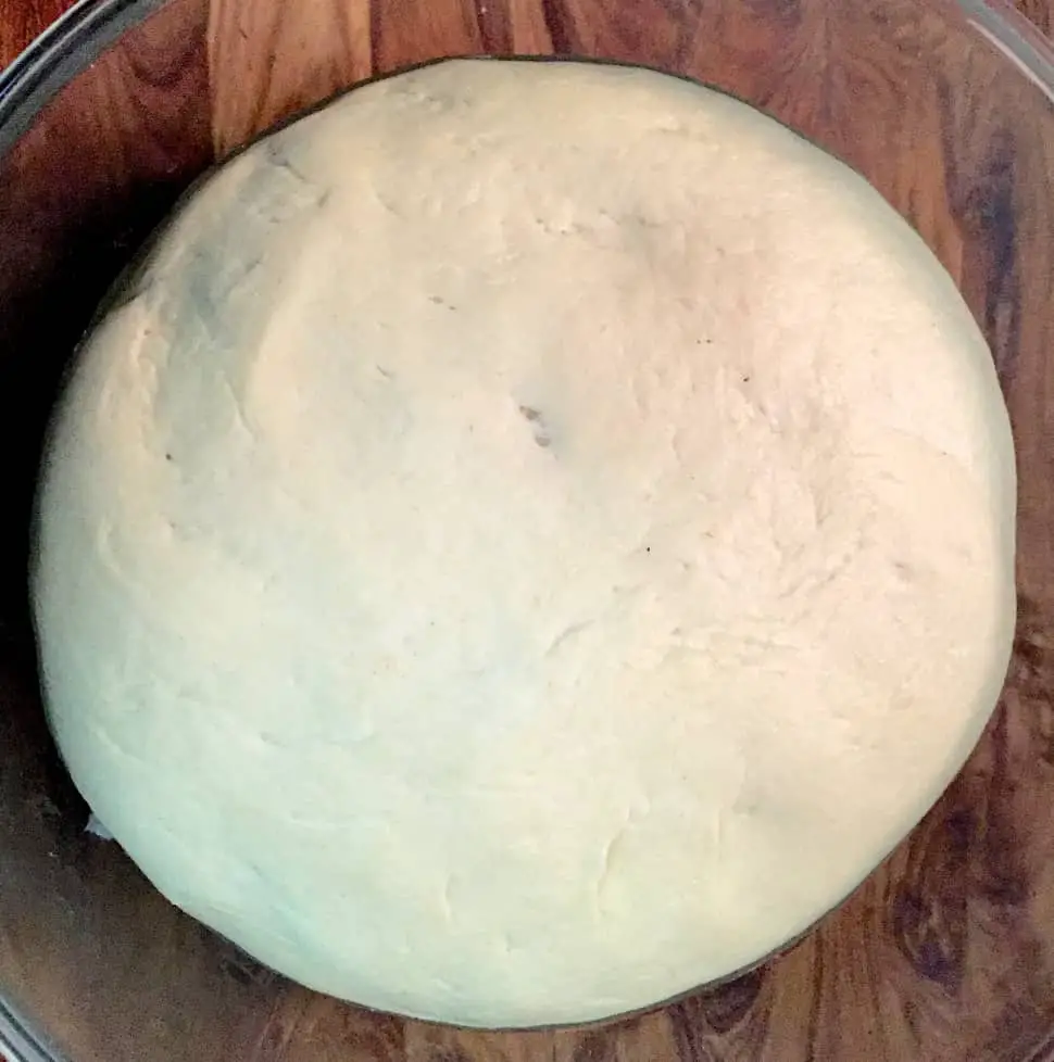 A round sphere of basic Dough for pizza, rising in a glass bowl on a brown wooden background