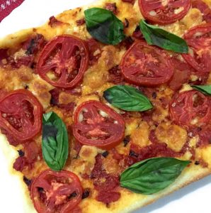 Thin crust tomato mozzarella pizza with slices of red tomato, mozzarella cheese and fresh basil leaves