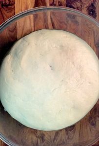 A round ball of Basic Pizza Dough in a glass bowl on a wooden background,just risen before it can be rolled into thin crust pizza
