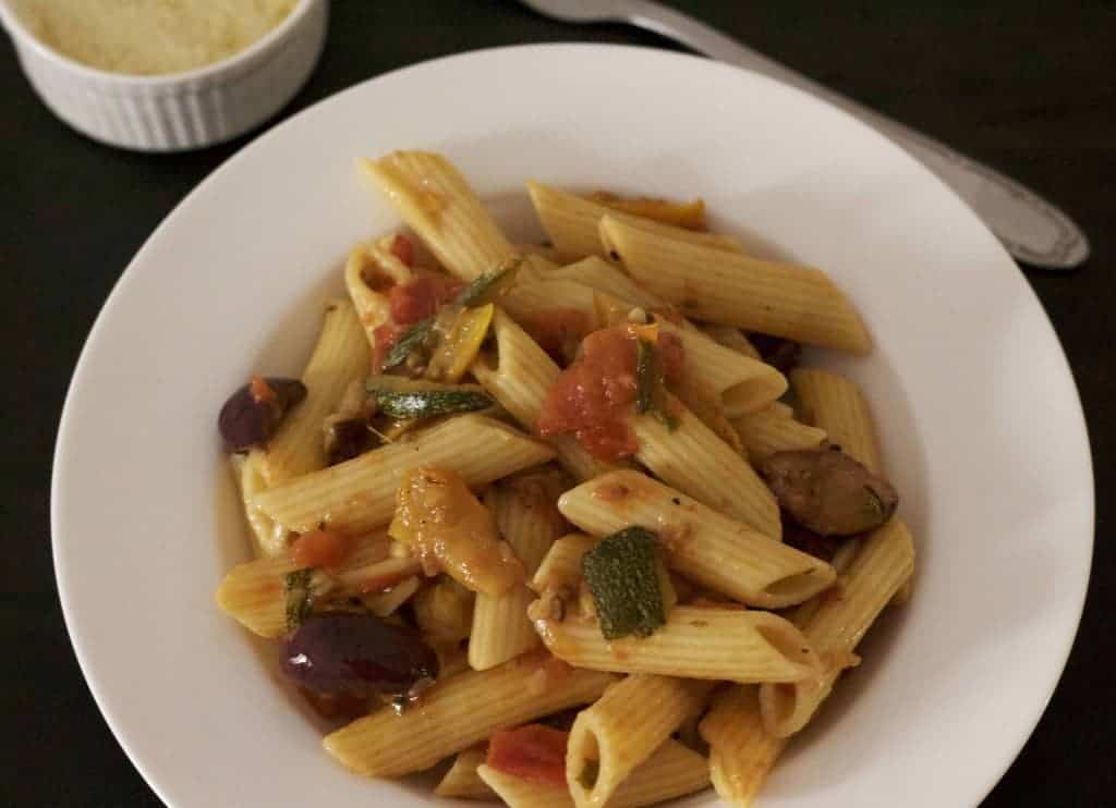 A white pasta plate of penne pasta with zucchini slices and tomato sauce