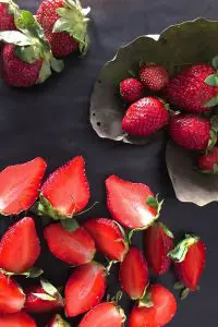 Bright red strawberries on a dried leaf and more strawberries on a black background