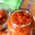 Reddish orange Pasta sauce in a glass jar with a cookbook and a green and white napkin in the background along with a bowl of sauce.