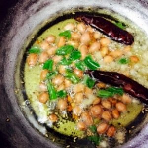 Process: a pan with gingelly oil in which mustard, chili, peanuts, curry leaves are being tempered