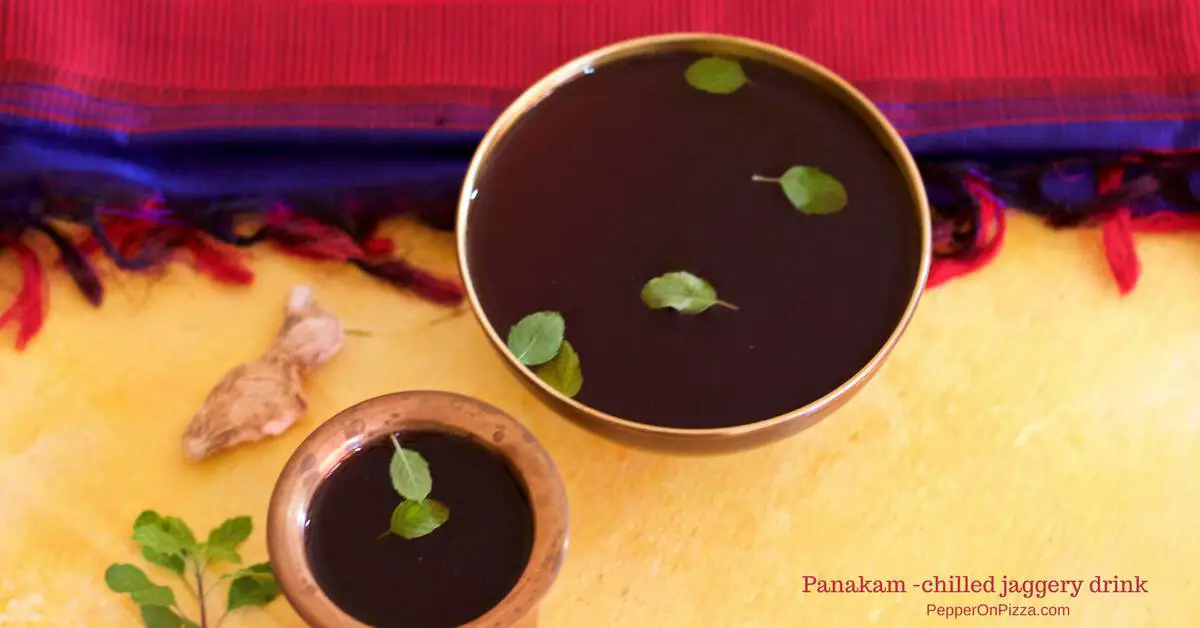 A brass bowl and brass tumbler filled with jaggery water or panakam garnished with green sacred basil and with a pink fabric in the background