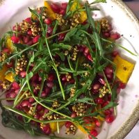 Yellow Roasted Pumpkin with green Rocket leaves and pink pomegranate on a white plate