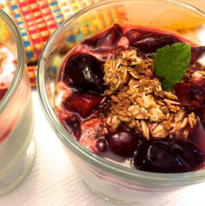 Tall glasses yogurt fresh cherry parfait topped with granola, mint leaves and homemade cherry compote and