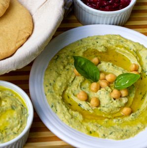 Pale green fresh lemon basil hummus garnished with chickpeas, olive oil and basil leaves, in a white plate